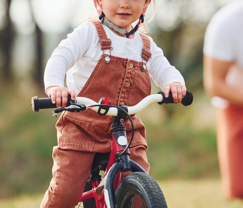 A father watches his daughter learn to ride a bicycle in the park